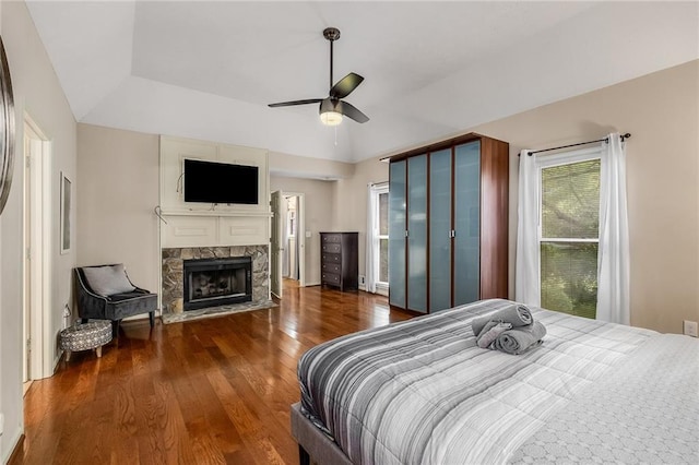 bedroom featuring dark wood-type flooring, ceiling fan, and a stone fireplace