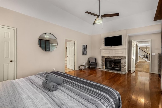 bedroom with lofted ceiling, dark hardwood / wood-style flooring, ceiling fan, and a stone fireplace