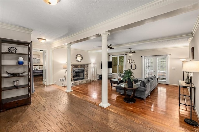 living room featuring ceiling fan, a stone fireplace, wood-type flooring, and decorative columns