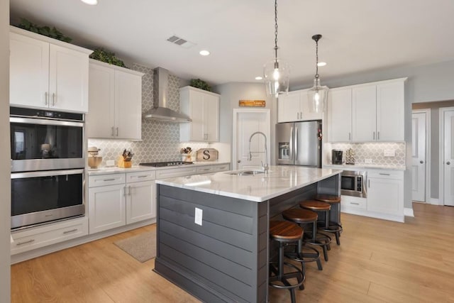 kitchen with appliances with stainless steel finishes, wall chimney range hood, white cabinets, decorative backsplash, and a sink