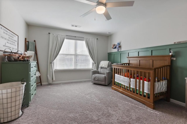 carpeted bedroom featuring a ceiling fan, visible vents, and a nursery area