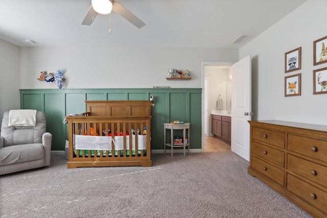 bedroom with a ceiling fan, a wainscoted wall, visible vents, a decorative wall, and light colored carpet