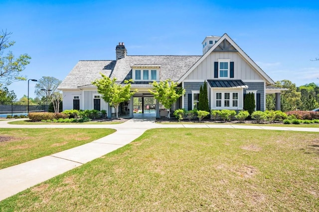 modern farmhouse featuring board and batten siding, a front lawn, a standing seam roof, and a chimney