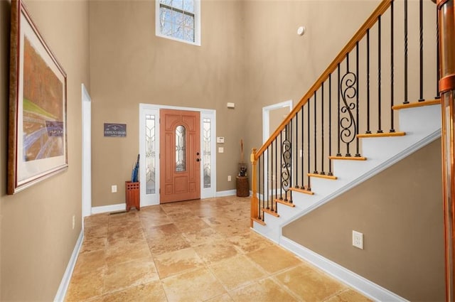 foyer entrance with stairs, baseboards, and a towering ceiling