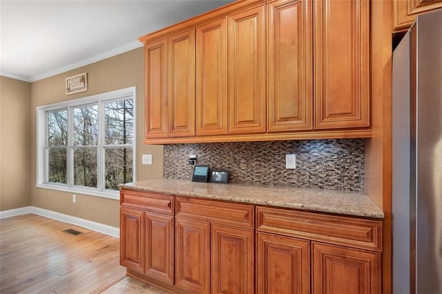 kitchen featuring decorative backsplash, brown cabinetry, freestanding refrigerator, and ornamental molding