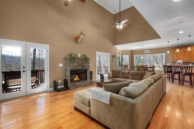 living area with a high ceiling, a fireplace, ceiling fan, light wood-style floors, and french doors