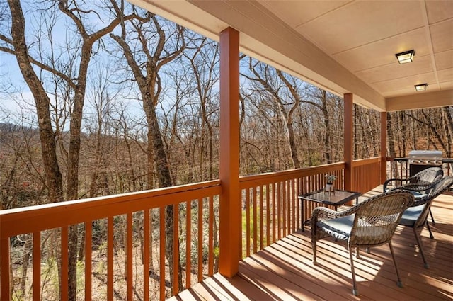 wooden deck featuring a view of trees and a grill