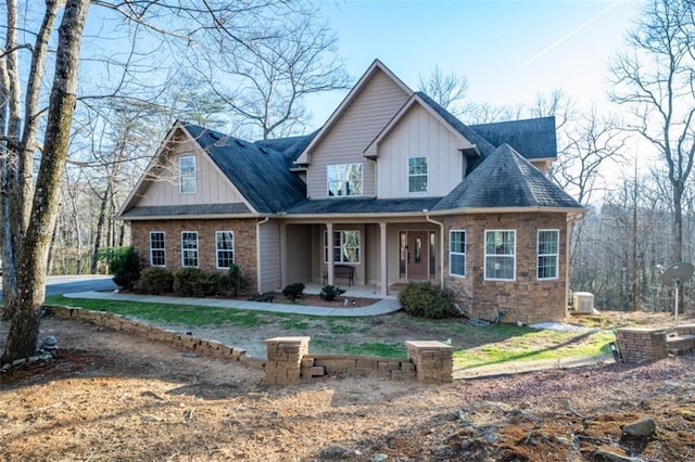 view of front facade featuring stone siding, a porch, a shingled roof, and board and batten siding