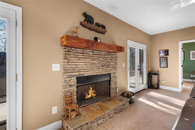 living area featuring a stone fireplace, french doors, baseboards, and carpet