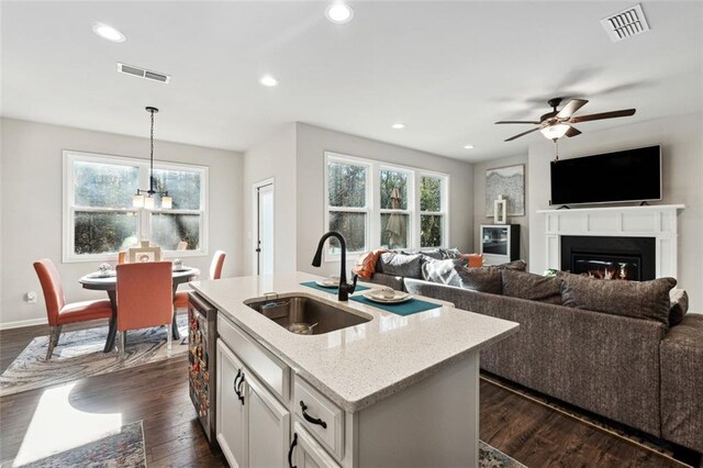 kitchen featuring light stone countertops, sink, dark hardwood / wood-style flooring, pendant lighting, and a center island with sink