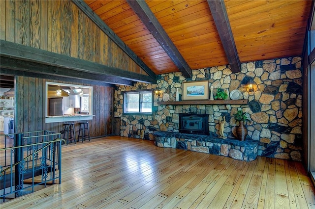 unfurnished living room with a stone fireplace, vaulted ceiling with beams, wooden ceiling, wooden walls, and light hardwood / wood-style floors