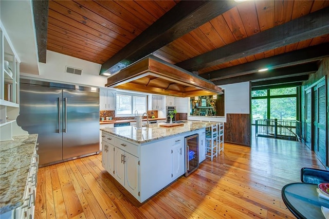 kitchen featuring wine cooler, white cabinetry, light stone counters, built in refrigerator, and a kitchen island