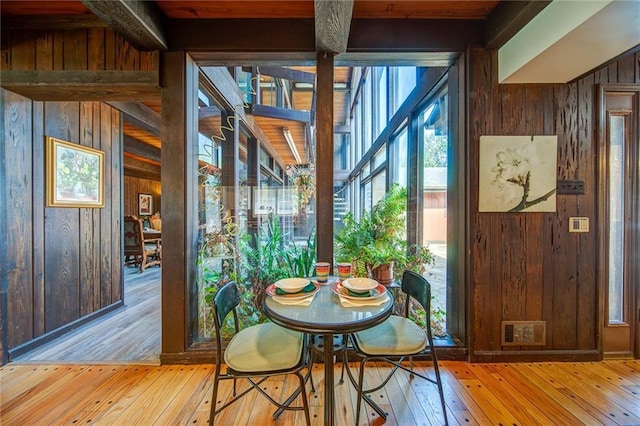 dining area with wooden walls, beamed ceiling, and light wood-type flooring