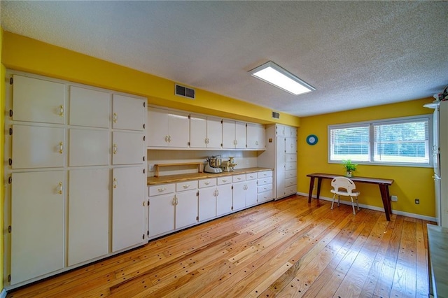 kitchen featuring a textured ceiling, white cabinets, and light wood-type flooring