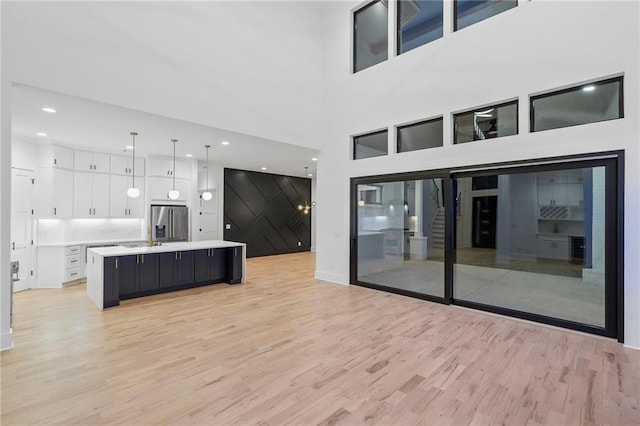 kitchen featuring pendant lighting, white cabinetry, an island with sink, stainless steel fridge with ice dispenser, and light wood-type flooring