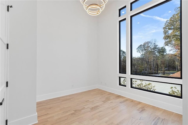 empty room featuring a notable chandelier, a healthy amount of sunlight, and light wood-type flooring