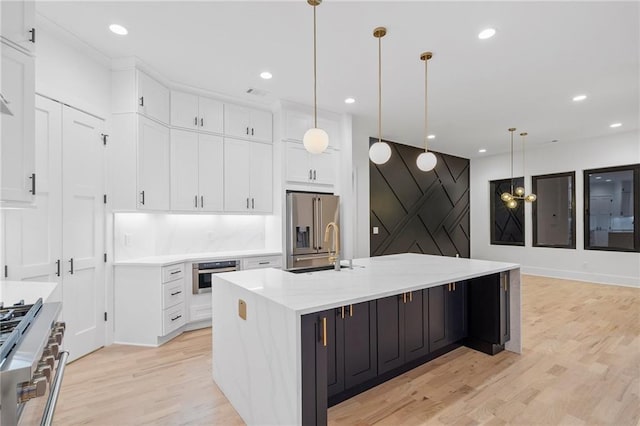 kitchen featuring stainless steel appliances, white cabinetry, pendant lighting, and a center island with sink