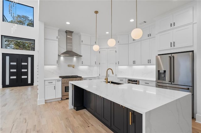 kitchen featuring high end appliances, white cabinetry, a large island with sink, and wall chimney exhaust hood