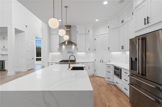 kitchen featuring white cabinetry, high quality fridge, decorative light fixtures, and wall chimney range hood