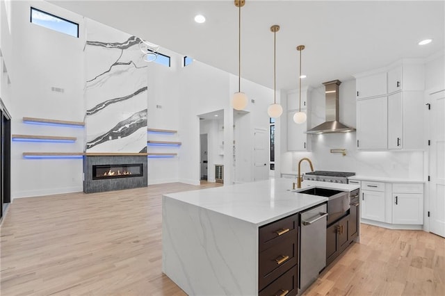 kitchen with wall chimney exhaust hood, light hardwood / wood-style flooring, stainless steel dishwasher, pendant lighting, and white cabinets