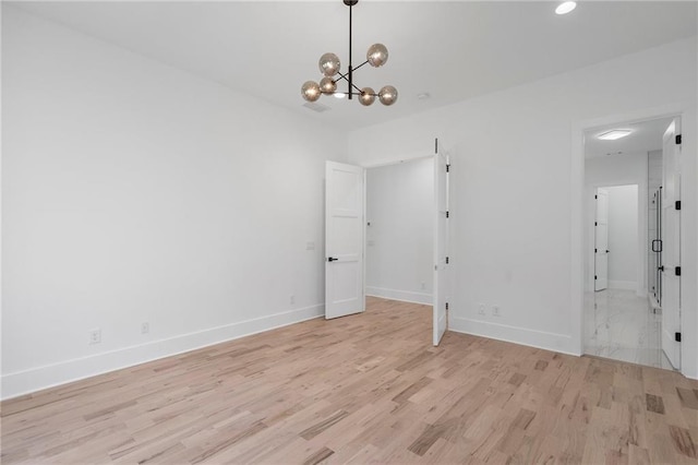 spare room with an inviting chandelier and light hardwood / wood-style flooring