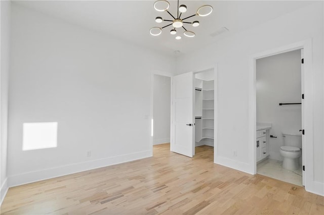 unfurnished bedroom featuring an inviting chandelier, a walk in closet, ensuite bath, light hardwood / wood-style flooring, and a closet