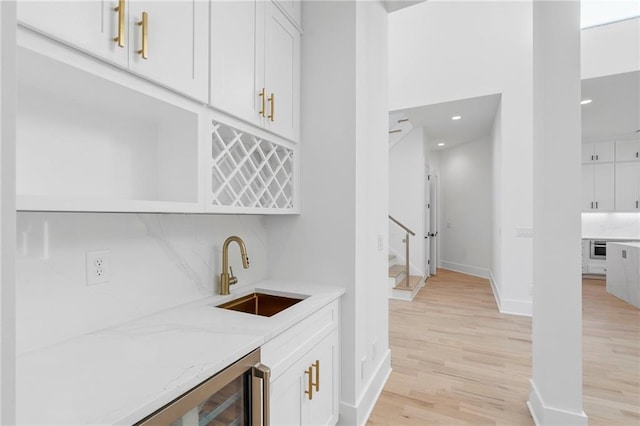 bar featuring sink, light hardwood / wood-style flooring, white cabinetry, backsplash, and light stone counters