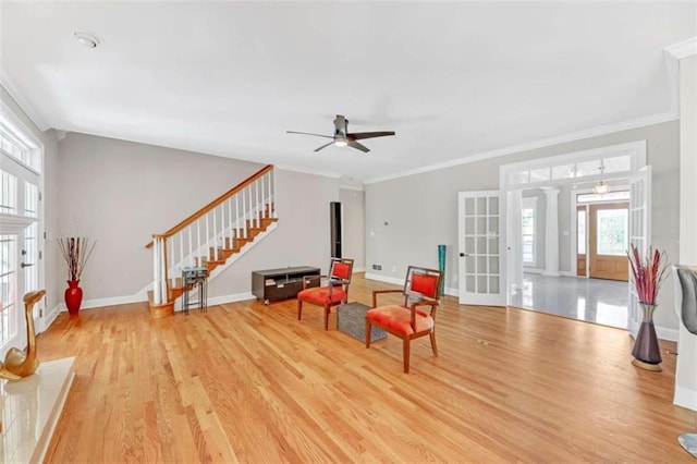 living area with ceiling fan, light wood-style floors, stairs, baseboards, and ornamental molding