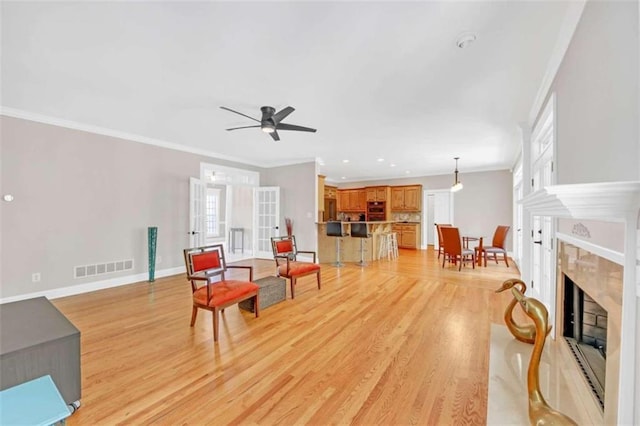 living room featuring light wood-type flooring, a fireplace, crown molding, recessed lighting, and a ceiling fan