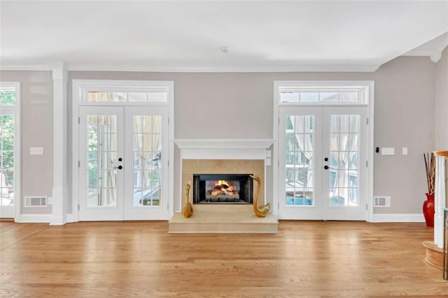 unfurnished living room with french doors, crown molding, wood finished floors, baseboards, and a fireplace