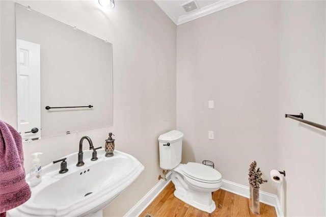 bathroom with a sink, wood finished floors, toilet, baseboards, and crown molding