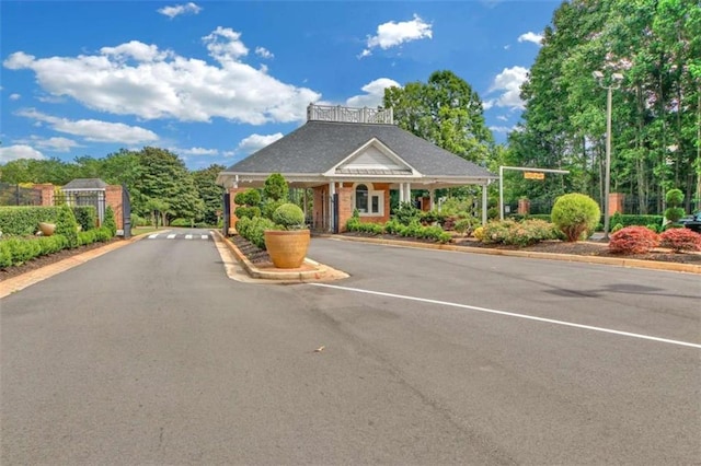 view of asphalt street with a gate, a gated entry, and curbs