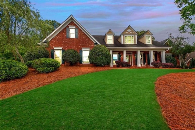 view of front of property featuring a porch, a lawn, and brick siding