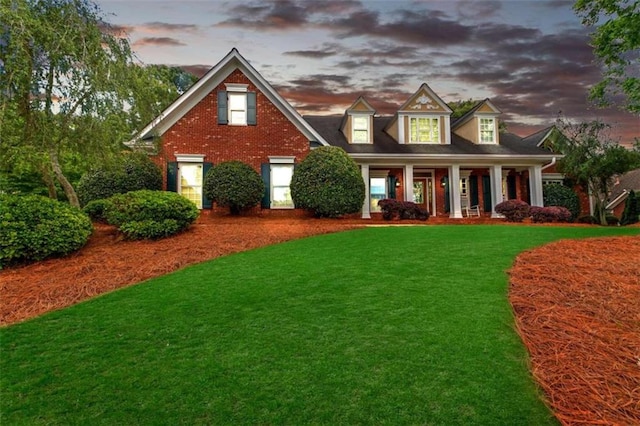 view of front of house with covered porch, a lawn, and brick siding