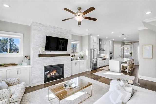 living area featuring crown molding, recessed lighting, a fireplace, and dark wood-style flooring