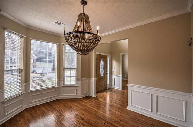 unfurnished dining area featuring an inviting chandelier, crown molding, dark wood-type flooring, and a textured ceiling