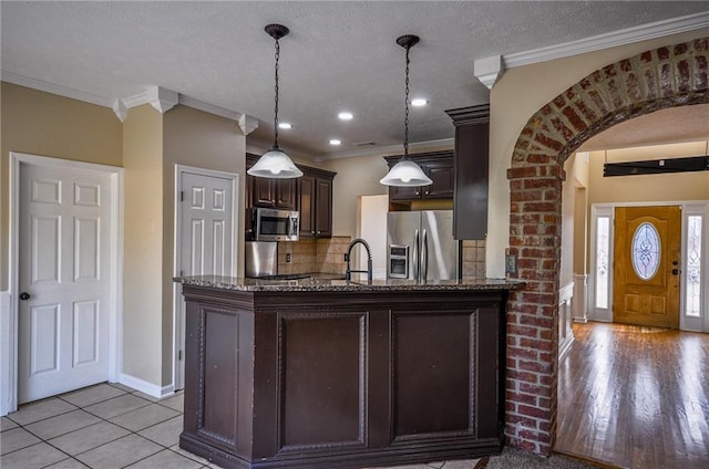 kitchen featuring tasteful backsplash, crown molding, dark brown cabinets, pendant lighting, and stainless steel appliances