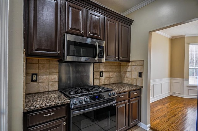 kitchen with dark wood-type flooring, dark brown cabinetry, ornamental molding, appliances with stainless steel finishes, and dark stone counters