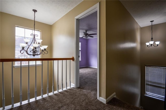 corridor with dark carpet, a wealth of natural light, a textured ceiling, and a chandelier