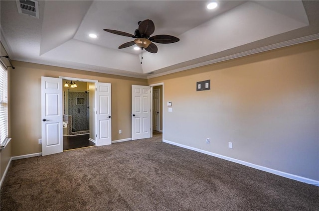 unfurnished bedroom featuring multiple windows, dark carpet, a raised ceiling, and ensuite bathroom