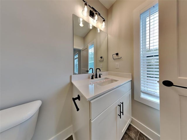 half bathroom with a healthy amount of sunlight, toilet, vanity, and baseboards