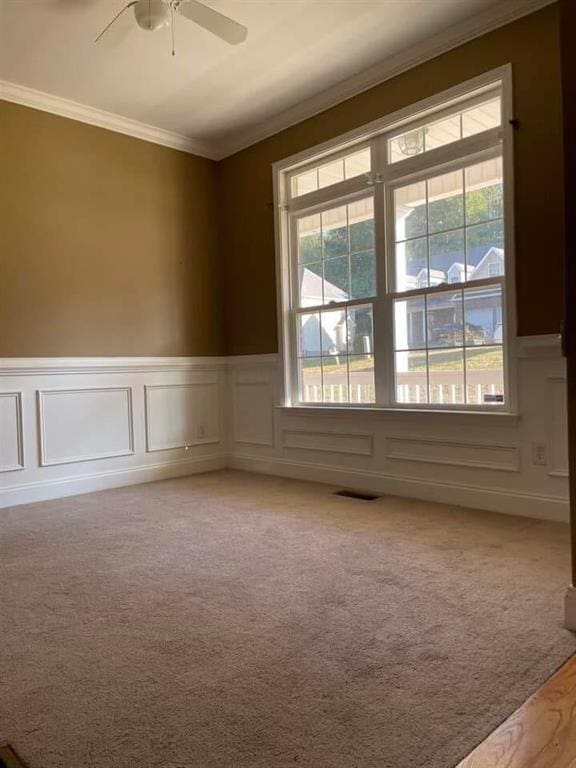 unfurnished room with plenty of natural light, light colored carpet, visible vents, and ornamental molding