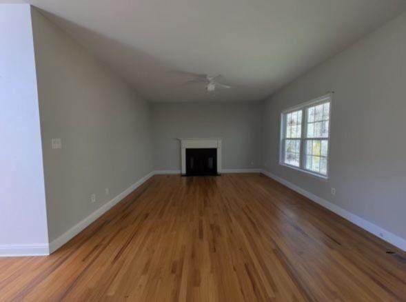 unfurnished living room featuring wood finished floors, baseboards, a fireplace with flush hearth, and ceiling fan