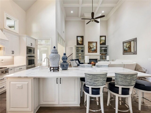5964 Chickasaw Ln, Braselton, GA 30517 - kitchen with coffered ceiling, stainless steel appliances, a sink, a towering ceiling, and a glass covered fireplace
