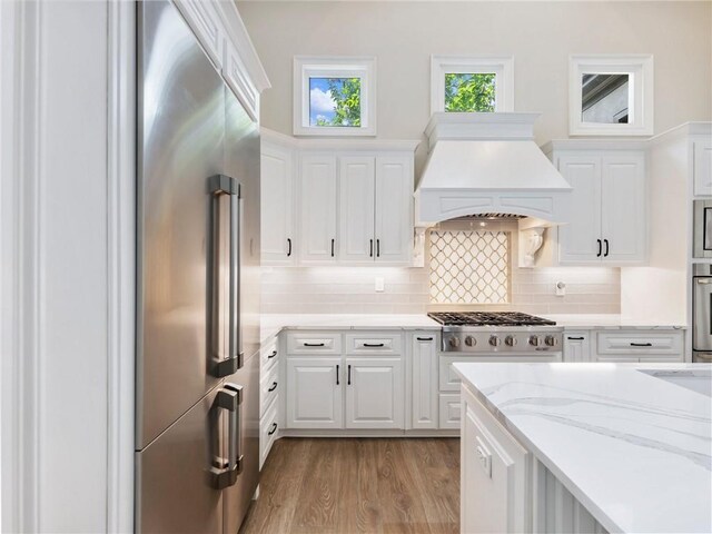 5964 Chickasaw Ln, Braselton, GA 30517 - kitchen with backsplash, white cabinetry, light wood-type flooring, stainless steel appliances, and custom range hood