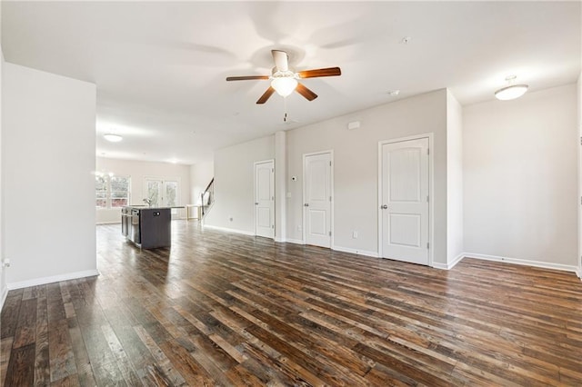 unfurnished living room featuring ceiling fan with notable chandelier and dark hardwood / wood-style floors