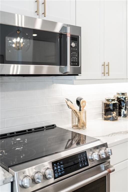 interior space with light stone counters, white cabinetry, stainless steel appliances, and backsplash