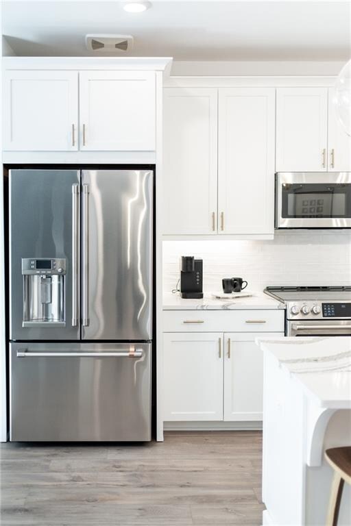 kitchen with light wood-type flooring, light stone counters, stainless steel appliances, white cabinets, and backsplash