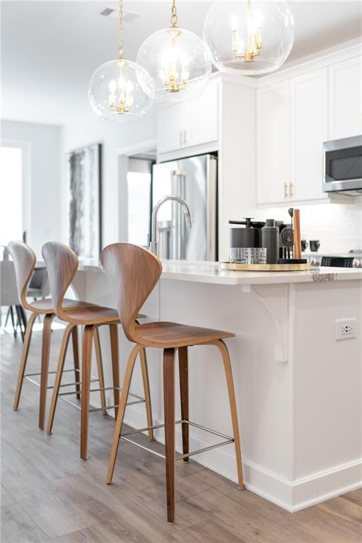 kitchen featuring white cabinets, decorative light fixtures, stainless steel appliances, a kitchen breakfast bar, and light hardwood / wood-style floors