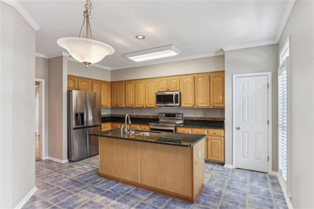 kitchen featuring dark stone counters, an island with sink, ornamental molding, a sink, and appliances with stainless steel finishes